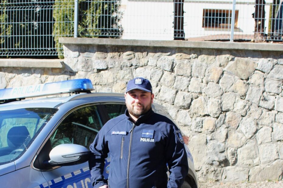 Piotr Kiliański w policyjnym mundurze przy radiowozie